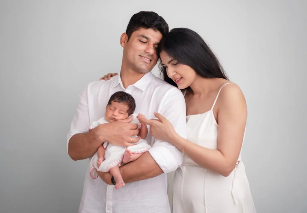 Happy family portrait with parents and baby in a white-themed professional photoshoot at Say Cheese Ranchi studio