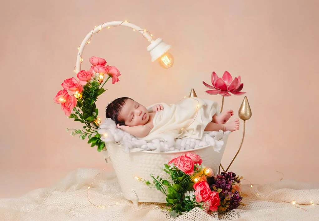 Newborn baby sleeping peacefully in a floral basket with fairy lights during a professional photoshoot at Say Cheese studio in Ranchi